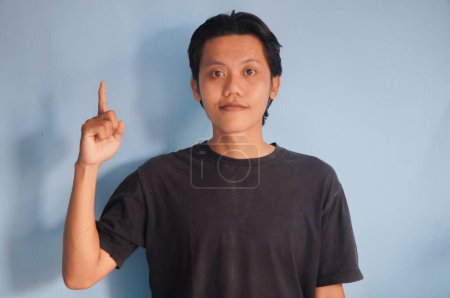 Photo for Young asian man wearing black t-shirt smiling pointing with hand finger to the up - Royalty Free Image