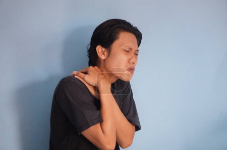 Junger asiatischer Mann berührt seine Schulter mit Schmerzausdruck