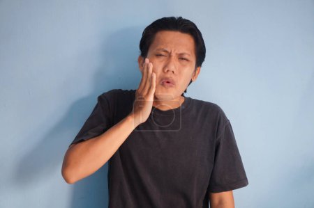 Asiatischer junger Mann im schwarzen T-Shirt mit Zahnschmerz-Gesichtsausdruck.