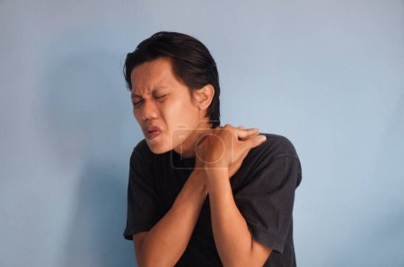 Junger asiatischer Mann berührt seine Schulter mit Schmerzausdruck