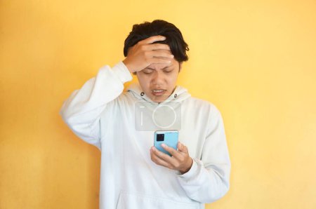 Asiático joven mostrando confusa expresión facial mientras sostiene el teléfono móvil