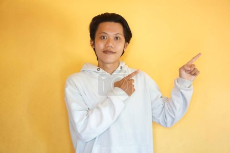 Photo for Asian young man wearing a hoodie excited pointing with hand finger up - Royalty Free Image
