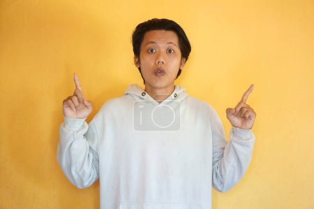 Photo for Asian young man wearing a hoodie excited pointing with hand finger up - Royalty Free Image