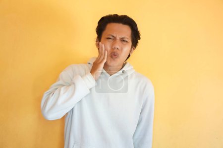 Asiatischer junger Mann trägt Kapuzenpullover mit Zahnschmerzen-Gesichtsausdruck.