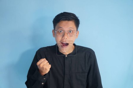 Foto de Asiático joven hombre usando gafas apretado puño mostrando éxito gesto - Imagen libre de derechos