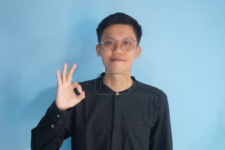 Asiatique jeune homme portant des lunettes souriant heureux tout en donnant "OK signe"