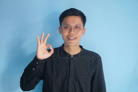 Téléchargez les photos : Asiatique jeune homme portant des lunettes souriant heureux tout en donnant "OK signe" - en image libre de droit