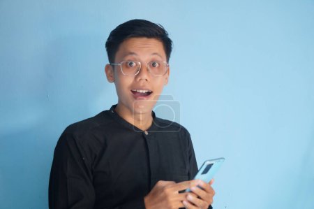 Photo for Young asian man showing happy face expression when holding mobile phone - Royalty Free Image