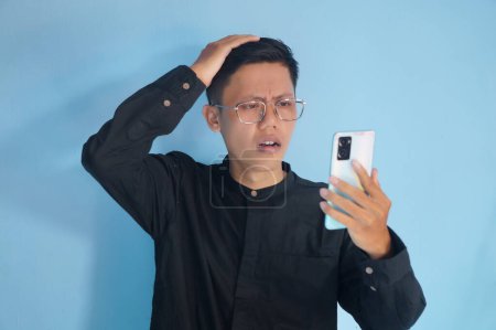 Junger Asiate zeigt verwirrten Gesichtsausdruck, während er Handy hält