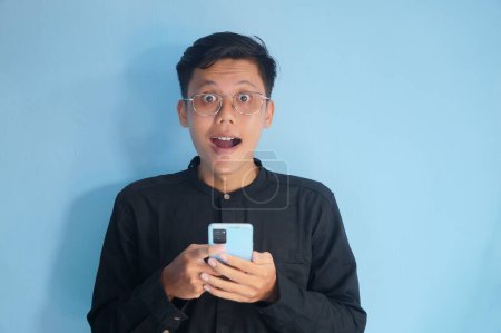 Photo for Young asian man showing happy face expression when holding mobile phone - Royalty Free Image