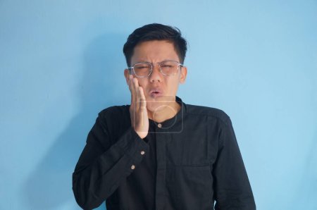 Asiatischer junger Mann im schwarzen Hemd mit Zahnschmerzen-Gesichtsausdruck.
