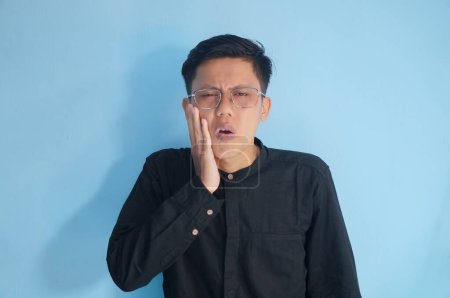 Asian young man in black shirt with toothache expression.
