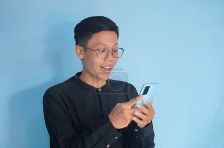 Photo for Asian young man looking at his mobile phone with amazed expression - Royalty Free Image