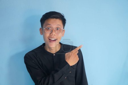 Ein hübscher asiatischer Mann im schwarzen Hemd zeigt mit dem Finger nach oben auf einen leeren Raum. Option, Empfehlung, Präsentation aufzeigen