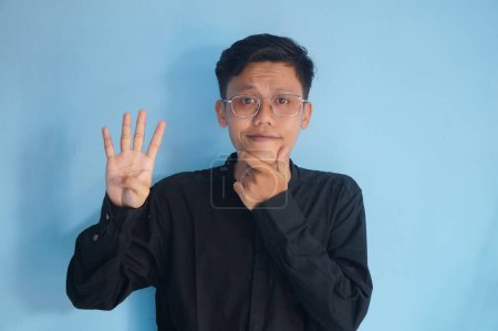Photo for Asian young man wearing a black shirt showing curious face expression while giving four fingers sign - Royalty Free Image