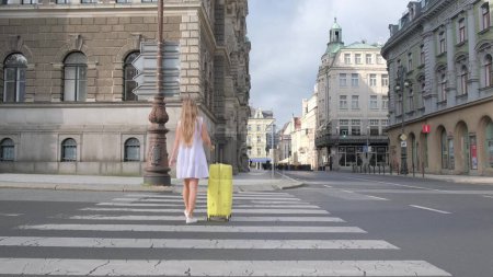 Photo for Beautiful female tourist walking with a suitcase on the street in a European city, tourism in Europe. Travel around the world - Royalty Free Image