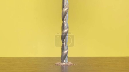 Photo for A self-tapping screw in a wooden block on a yellow background. Screwdriver screw lag bolt. The electric drill screws the bolt into the wooden surface. - Royalty Free Image