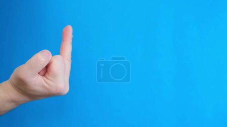 Téléchargez les photos : Gros plan du geste négatif de la main majeur doigt vers le haut sur fond bleu. - en image libre de droit
