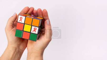 Téléchargez les photos : Rubiks Cube avec ruban rouge sida dans la main des femmes. Symbole de la Journée mondiale du sida, Mois de la sensibilisation au VIH... - en image libre de droit