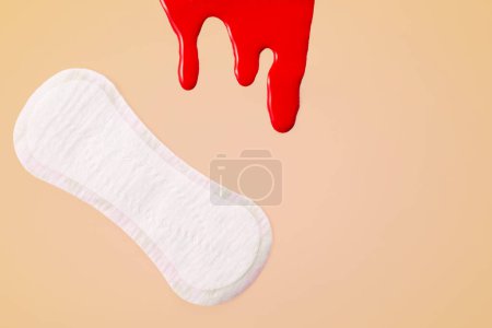 Blood and feminine hygiene pad on peach background. First menstrual period concept.
