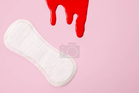 Blood and feminine hygiene pad on pink background. First menstrual period concept.