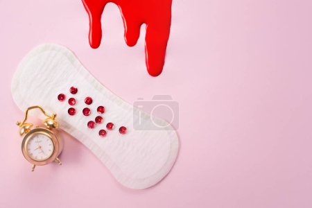 Sang et coussin hygiénique féminin avec paillettes rouges sur fond rose. Première période menstruelle concept.