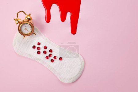 Blood and feminine hygiene pad with red glitter on pink background. First menstrual period concept.