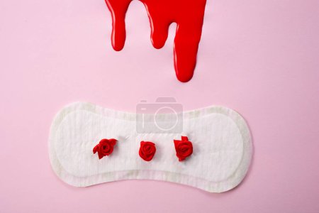 Blood and feminine hygiene pad with red flowers on pink background. First menstrual period concept.