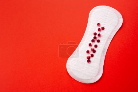 Feminine hygiene pad with red glitter on red background. First menstrual period concept, menstruation cycle period.