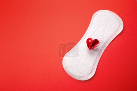 Feminine hygiene pad with red heart on pink background. First menstrual period concept, menstruation cycle period.