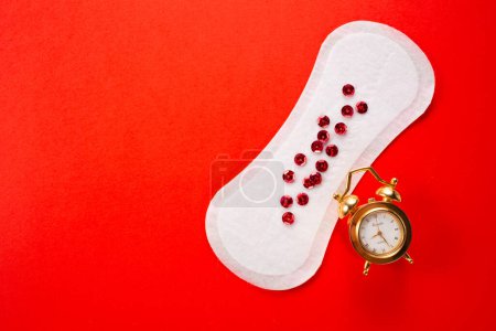 Alarm clock and feminine hygiene pad with red glitter on red background. First menstrual period concept.