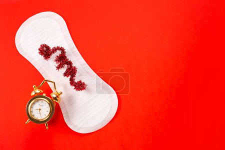 Alarm clock and feminine hygiene pad on red background. First menstrual period concept, menstruation cycle period.