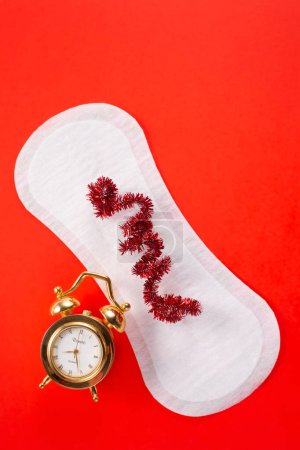 Alarm clock and feminine hygiene pad on red background. First menstrual period concept, menstruation cycle period.
