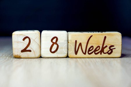 Téléchargez les photos : 28 semaines de grossesse âge jalon écrit sur un cube en bois avec un fond noir - en image libre de droit