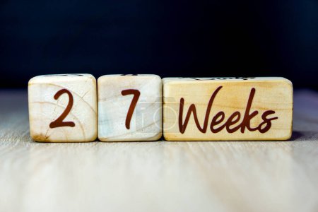 Téléchargez les photos : 27 semaines de grossesse âge jalon écrit sur un cube en bois avec un fond noir - en image libre de droit