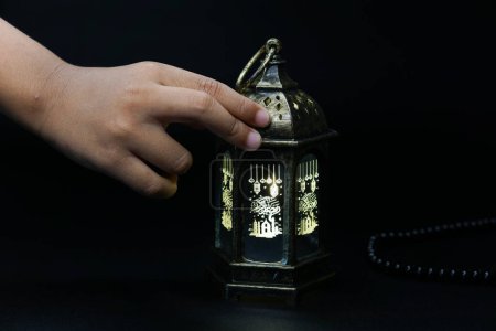 Ramadan Kareem, the hand holding the lantern on a black background