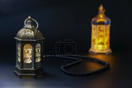 Ramadan Kareem, two lanterns and prayer beads on a black background