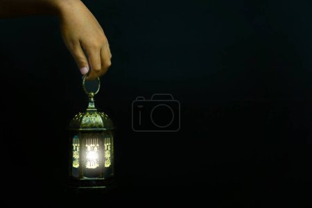 Ramadan Kareem, the hand holding the lantern on a black background