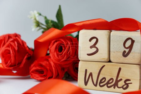 Téléchargez les photos : 39 semaines d'âge gestationnel jalon écrit sur un cube en bois avec des roses rouges et des rubans, et un fond blanc - en image libre de droit