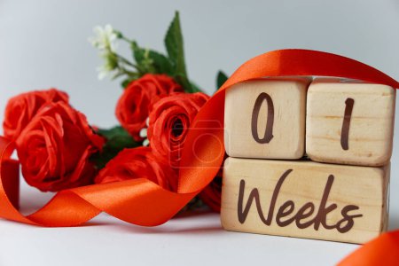 Téléchargez les photos : Jalon de l'âge gestationnel d'une semaine écrit sur un cube en bois avec des roses rouges et des rubans, et un fond blanc - en image libre de droit