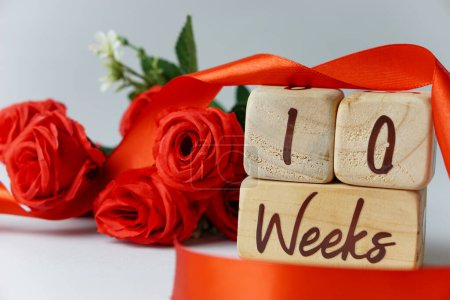 Téléchargez les photos : Jalon de l'âge gestationnel de 10 semaines écrit sur un cube en bois avec des roses rouges et des rubans, et un fond blanc - en image libre de droit