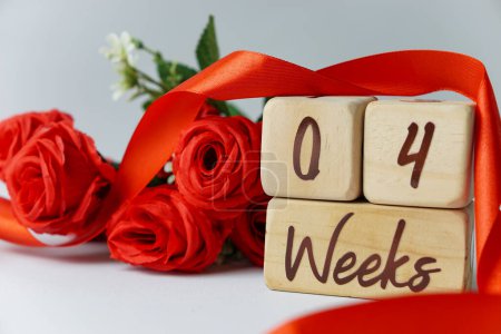 Téléchargez les photos : Jalon de l'âge gestationnel de 4 semaines écrit sur un cube en bois avec des roses rouges et des rubans, et un fond blanc - en image libre de droit