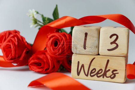 Téléchargez les photos : Jalon d'âge gestationnel de 13 semaines écrit sur un cube en bois avec des roses rouges et des rubans, et un fond blanc - en image libre de droit