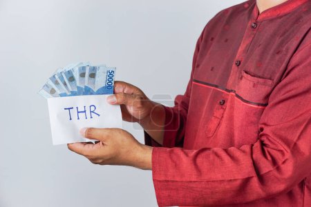 La main d'un Asiatique tenant une enveloppe THR contenant des billets de Rupiah. THR ou Tunjangan Hari Raya est une allocation de vacances ou un bonus donné pendant le mois de Ramadan.