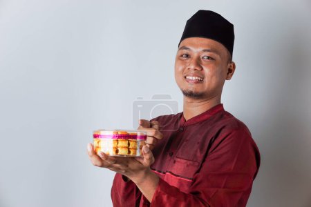 Porträt eines asiatischen muslimischen Mannes, der einen nastar-Keks hält und auf ihn zeigt