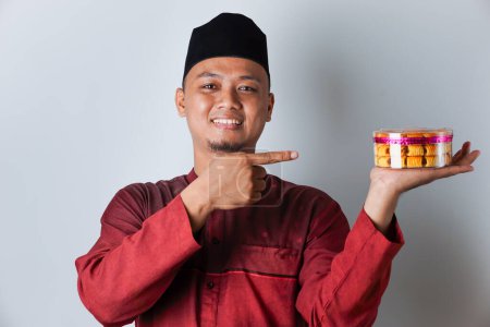 Portrait of an Asian Muslim man holding and pointing to a nastar cookie