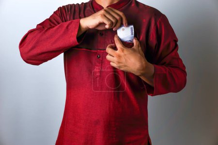 El gesto de un musulmán asiático tomando una nota de Rupiah de su bolsillo