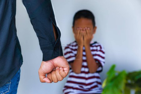 Photo for Violence against children. Cropped of man clenching his fists in anger, a small child crying and covering his face with his hands in the background. - Royalty Free Image