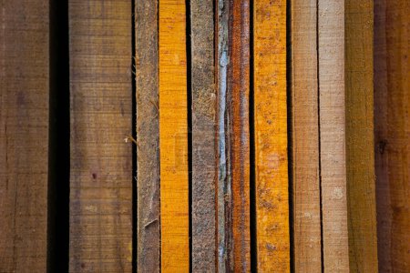 Varios tablones de madera en diferentes tonos y texturas se apilan cuidadosamente juntos, mostrando una gama de colores y granos de madera natural.