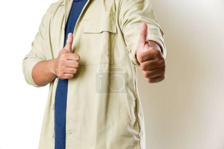 A person wearing a beige jacket and a blue shirt gives two thumbs up, expressing positivity and approval against a white background.